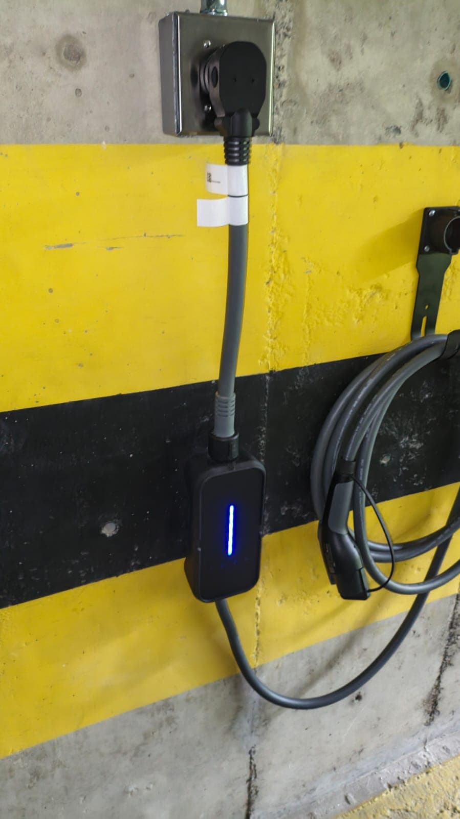 Equipo de carga portátil conectado a una toma de pared en un parqueadero