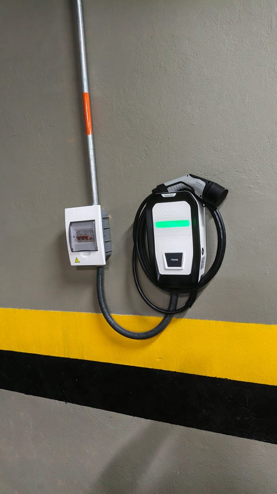 Cargador de pared y caja eléctrica conectados mediante canalización en un parqueadero